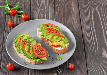 Avocado sandwich on ciabatta bread made with fresh sliced avocados and vegetables, from above. Healthy vegetarian breakfast on a dark wooden table.