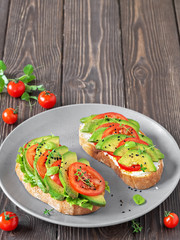 Avocado sandwich on ciabatta bread made with fresh sliced avocados and vegetables, from above. Healthy vegetarian breakfast on a dark wooden table. Closeup with copy space