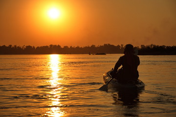 Naklejka na ściany i meble Man paddling in kayak during sunset on Mekong river