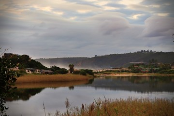 Cloudy sky over the Touws River mouth with reeds in the foreground and houses on the banks of the river