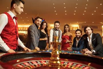 Group happy friends make bets gambiling at the roulette table in the casino.