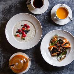 Menu at the cafe, Breakfast and lunch, Porridge with berries and pasta with seafood, Bulgur and black spaghetti with shrimps. Flatlay, Top view, Moody on black background, Darkstyle