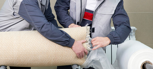 Men workers packing carpet in a plastic bag after cleaning it in automatic washing machine and dryer in the Laundry service