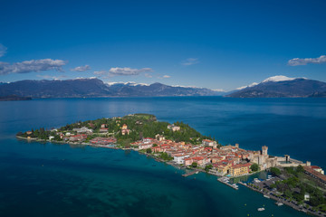 Fototapeta na wymiar Sirmione town, Lake Garda, Italy. Aerial view of Sirmione. The historical part of the city. In the background mountains in the snow and blue sky. Side view of the island.