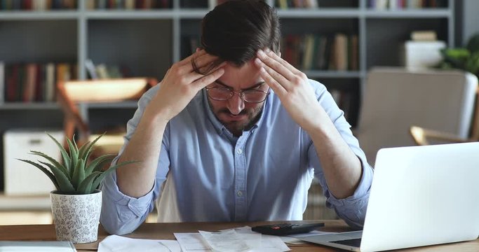 Depressed desperate man feeling worried about financial problem doing paperwork. Stressed businessman looking frustrated thinking of money debt, budget loss, bankruptcy sitting at home office desk.