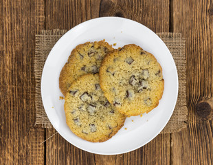 Old wooden table with fresh Chocolate Chip Cookies (close-up shot; selective focus)