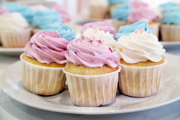 Mini cupcakes with whipped cream decorated with spring and Easter candy sprinkles. Additional cupcakes blurred in the background.
