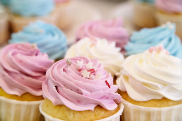 Mini cupcakes with whipped cream decorated with spring and Easter candy sprinkles. Additional cupcakes blurred in the background.