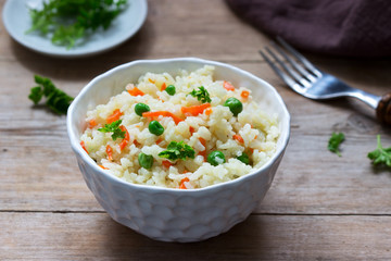 Vegetarian rice dish with vegetables and green peas on a wooden background.