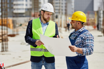 Two engineers discuss drafts they both hold.