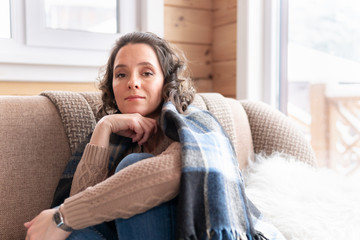 Woman sits and dreams on the sofa at home by the window