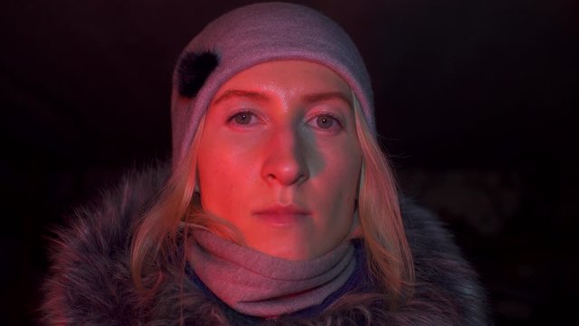 Portrait of shocked scared young woman. She is lit by police flashing lights and is talking on phone. woman is scared, desperately wants something, covering her mouth with hands of problem.
