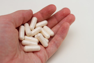 handful of pink capsule pills in hand on white background