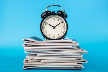 Newspapers and clock on blue background. Retro alarm clock on morning newspapers