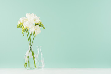 Fresh delicate white flowers freesia with funny glass vases  in green mint menthe interior on white wood board, copy space.