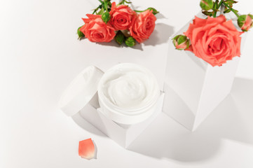 Cream in white unbranded container and roses decoration on background. Bottle with moisturizing professional skincare. Luxury cosmetics and beauty treatment concept.