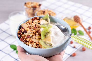 Healthy breakfast yogurt bowl with granola and fruits kiwi, banana. Hands holding bowl with yogurt and fruits