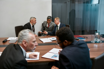 Multicultural business people in formal wear discussing contract conditions while having a meeting with partners in the modern office