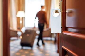 Expecting comfortable stay. Cropped shot of middle-aged businessman in casual wear with suitcase entering his room in the background. A door with a sign at the front.