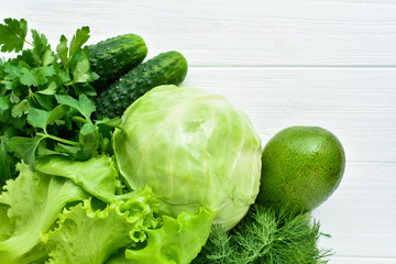 Green vegetables on white wooden background. Salad, cabbage, cucumber, dill, parsley, avocado View from above
