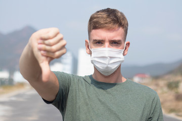 Serious European man, young guy in protective sterile medical mask on face look at camera show...