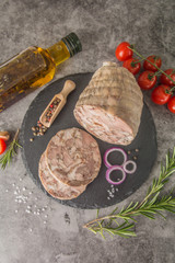 Brawn is a pressed pressed piece of meat cut on black slate. Top view, with spices, rosemary, tomato. Vertical photo.