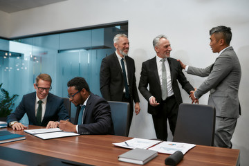 My congratulations. Two happy mature businessmen in classic wear shaking hands while having a multi-ethnic meeting in the modern office