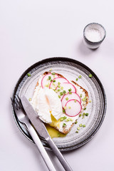 Open sandwich with radish, poached egg, cream cheese and green onion on a plate on grey concrete background. Selective focus