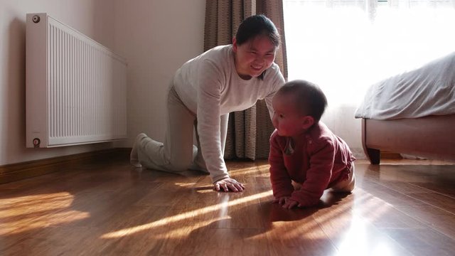 Slow motion of happy Chinese woman together with her little asian baby girl crawling on the floor with sun light coming from window in the bedroom happy child 4k footage mother and infant daughter joy