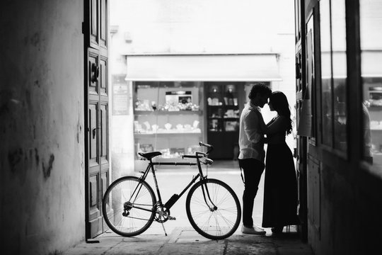 Photo session of love couple. A man and a woman are walking in the old city with a green retro bike. Black and white. Man and woman gently hugging in the alley