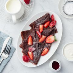 Chocolate crepes with fresh strawberry and powdered sugar on white plate
