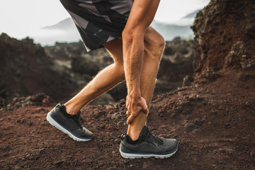 Male runner holding injured calf muscle and suffering with pain. Sprain ligament while running outdoors. Close-up legs view. - obrazy, fototapety, plakaty