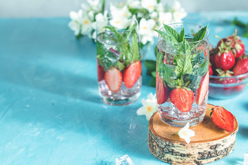 Detox infused water with strawberry and mint in highball glasses on blue concrete table background, copy space. Cold summer drink. Mineral water.