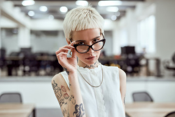 Young and succesful. Portrait of confident blonde tattooed businesswoman adjusting her eyeglasses...