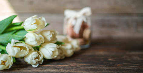 Spring flowers. Bouquet of white tulips and macaroons on brown wooden table. Mother's Day and Valentines Day background. Rustic style. Copy space for your text.