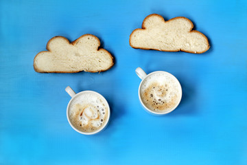 cups with cappuccino and buns on a blue background. coffee rain from bread clouds
