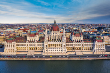 Fototapeta na wymiar Budapest, Hungary - Aerial drone view of the beautiful Hungarian Parliament building with warm colors at sunset. Afternoon traffic, River Danube, traditional yellow trams and blue sky at background