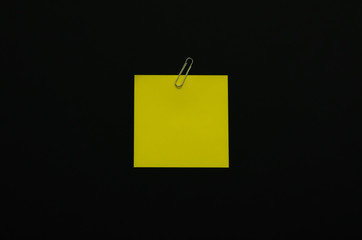 Yellow blank note paper with paper clip on dark background. Minimalist flat lay black concept.