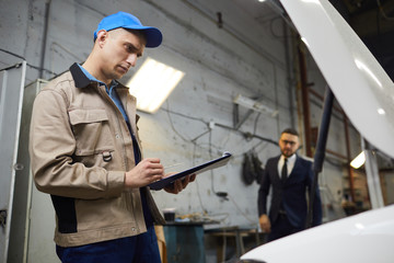 Professional car service worker checking vehicle health, his new client coming to him, horizontal low angle shot, copy space