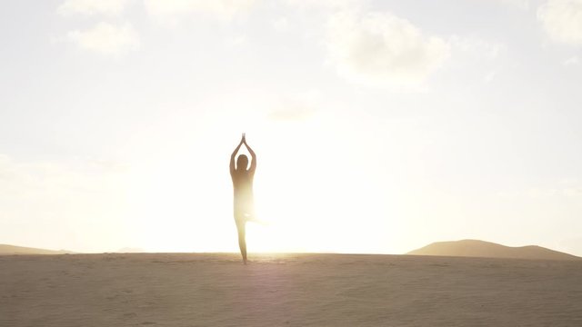 SLOW MOTION Mindfulness exercise in the desert with focus on breathing and stability. Young woman practicing yoga with arm movement. Tree pose at sunset in desert.