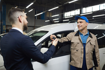Naklejka na ściany i meble Unrecognizable man wearing suit giving his car keys to auto service repairman, horizontal medium shot