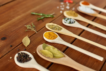 food, culinary and unhealthy eating concept - spoons with different spices and salt on wooden table