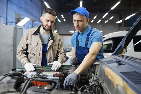 Horizontal medium shot of two young adult Caucasian men wearing uniform working together in auto service center