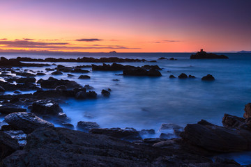 A rocky beach at sunset, with the sky glowing with rich orange and purple hues