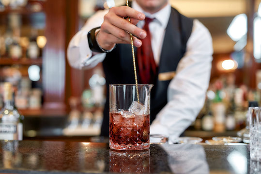 Excellent skills. Cropped shot of young bartender standing at counter and mixing ingredients while making iced cocktail in the bar