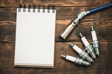 Spark plugs and blank page notepad with copy space on brown wooden workbench background.