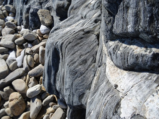 dark gray rocks seem to be flowing down to the pebbly beach
