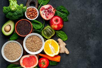 Selection of healthy food: fruits, seeds, cereals, superfoods, vegetables, leafy vegetables on a stone background. Healthy food for humans. Copy space for your text.