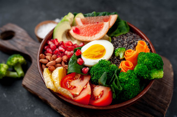 Bowl of Buddha,quinoa, orange, avocado, grapefruit, tomato, pomegranate, spinach, carrots, broccoli, egg in a bowl on a stone background, with copy space for your text
