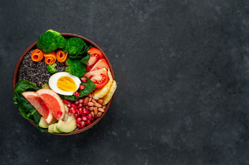 Fototapeta na wymiar Bowl of Buddha,quinoa, orange, avocado, grapefruit, tomato, pomegranate, spinach, carrots, broccoli, egg in a bowl on a stone background, with copy space for your text